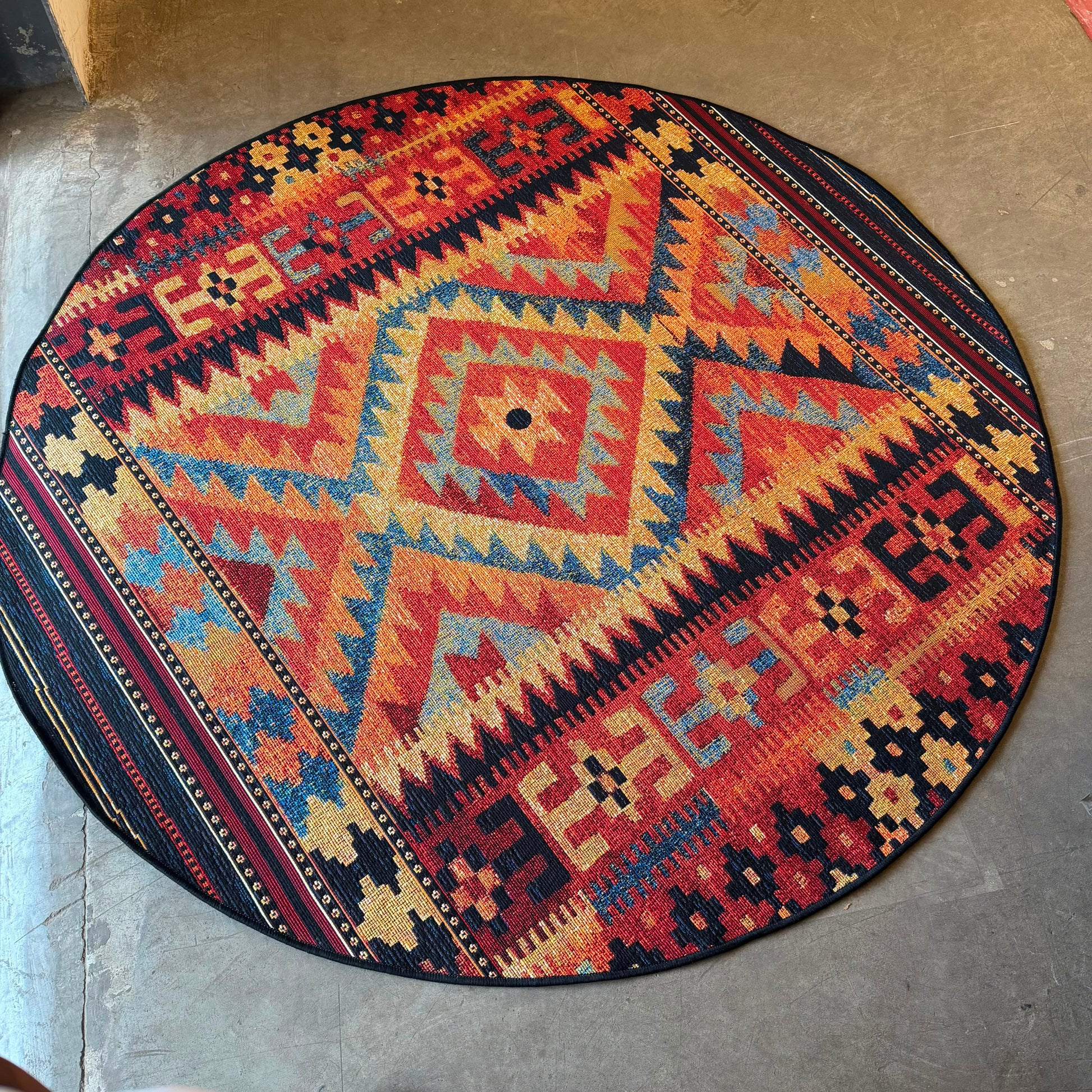 Oriental Weavers Isla round batik tribal geometric rug with red, orange, beige, navy, and blue pattern for indoor and outdoor spaces.