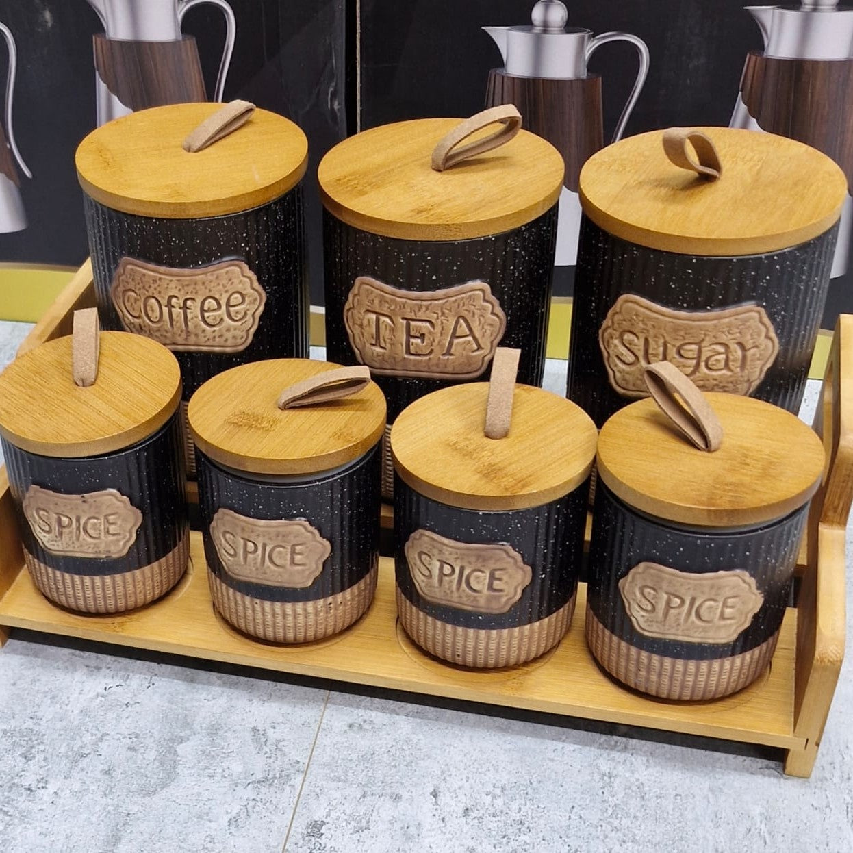 7 piece black ribbed ceramic canister set with wooden lids, leather handles, vintage labels, jute detailing, and two tier wooden stand for kitchen storage.