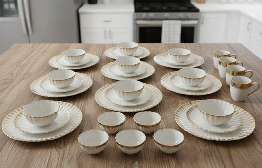 White ceramic shell dinner set with gold detailing including plates, bowls, cups, and saucers