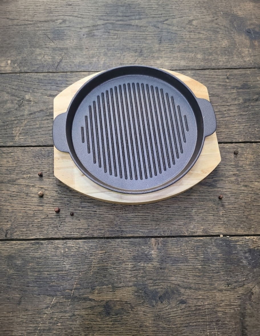 Round cast iron sizzling grill pan with wooden base for serving hot meals