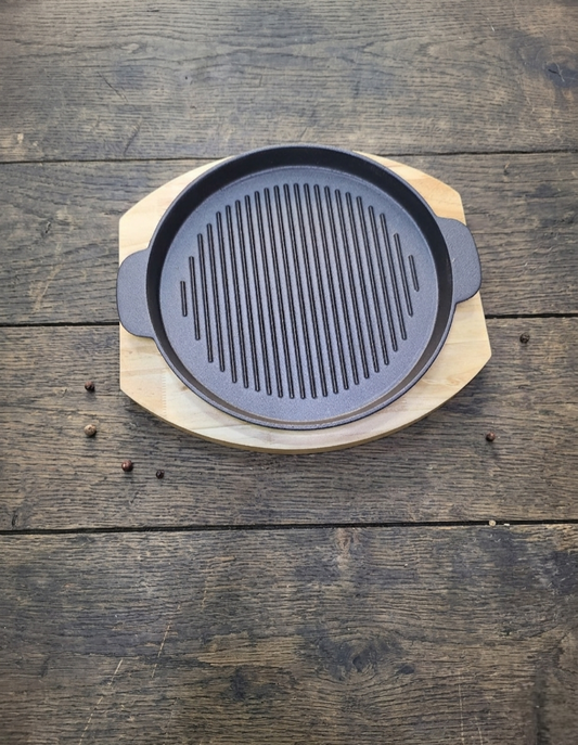 Round cast iron sizzling grill pan with wooden base for serving hot meals
