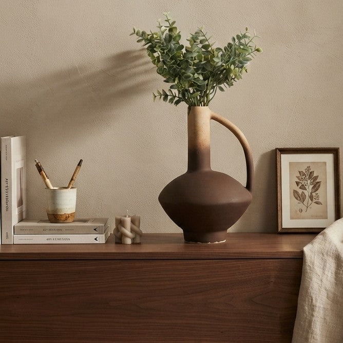 Two tone ceramic amphora vase with arched handle and dusty green artificial eucalyptus stems for interior décor.