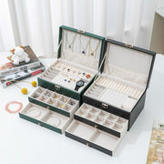 Multi layer jewelry storage box with embossed leather exterior and large capacity compartments in white, black, and green.