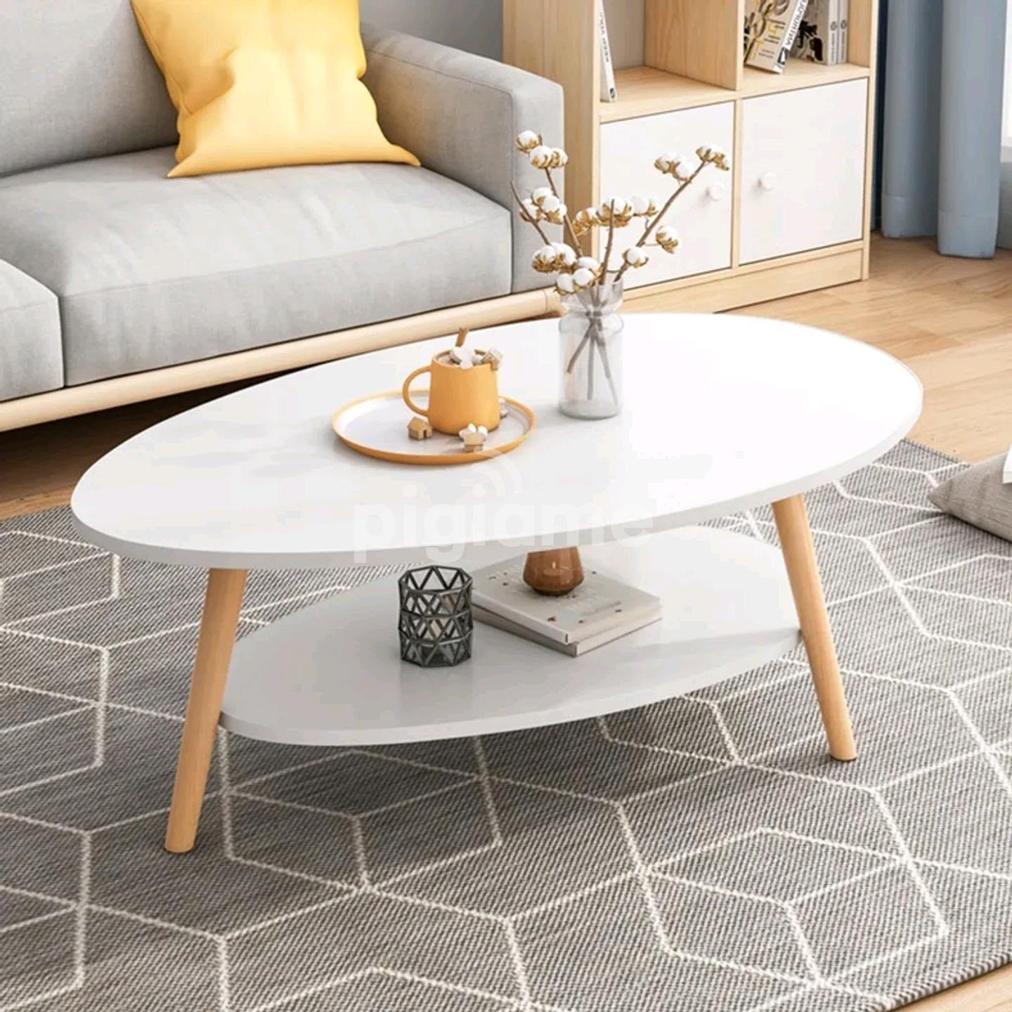 2 tier white oval coffee table with smooth egg shaped top, open lower storage shelf, and natural wood legs.