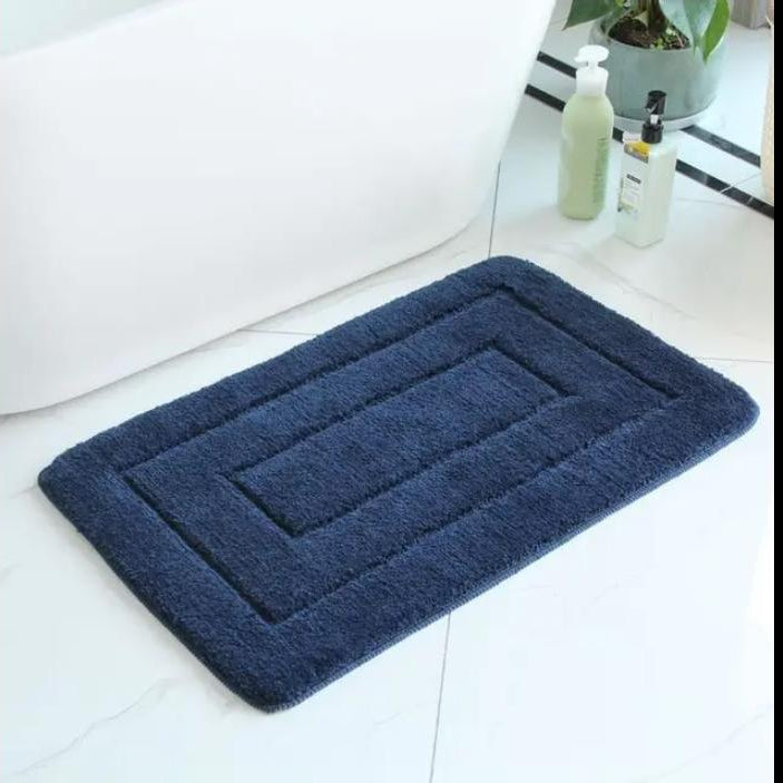 Plush beige non slip bath mat with absorbent textured surface and stepped border design for comfortable and safe bathroom use.