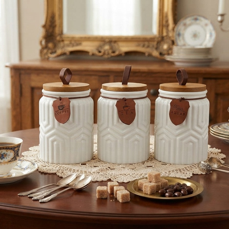 3 piece white ceramic canister set with geometric embossed design, bamboo lids, leather loop handles, labeled tags, and a wooden tray for kitchen storage.