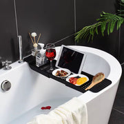 Expandable black bathtub caddy tray and organizer for holding books, phones, toiletries, and bath essentials.