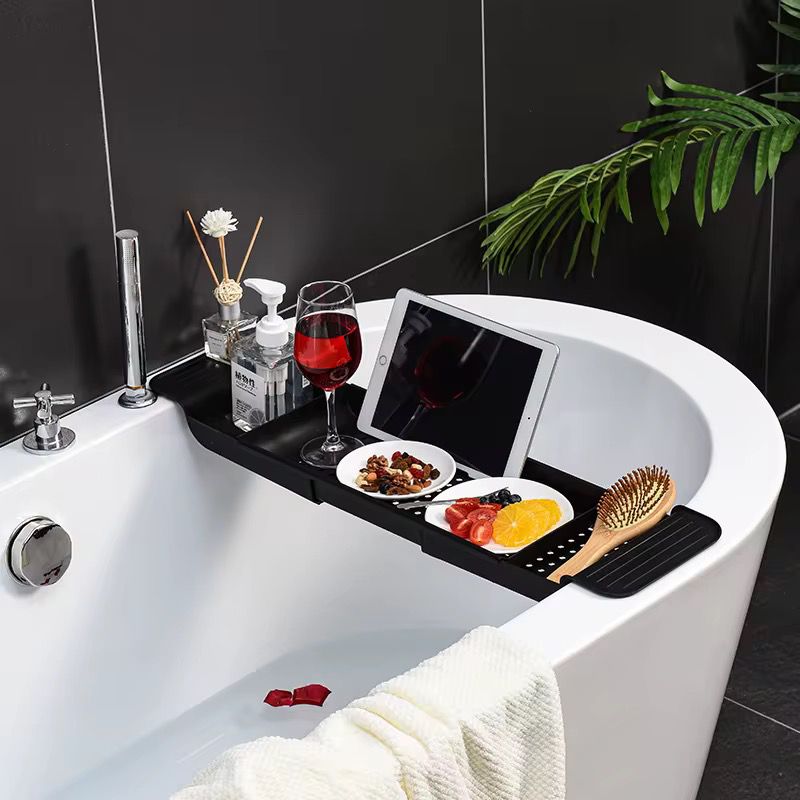 Expandable black bathtub caddy tray and organizer for holding books, phones, toiletries, and bath essentials.