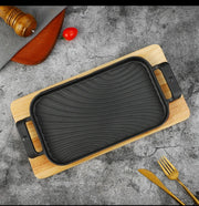 Rectangular cast iron sizzling grill pan with wooden base for serving hot meals
