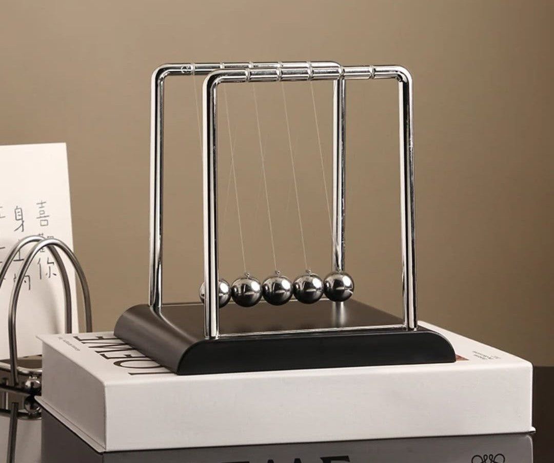 Newton’s cradle desk ornament with swinging steel balls demonstrating motion and balance, ideal for office or study desk décor. ⚙️