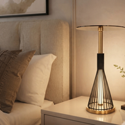 Caged bedside table lamp with black metal cage shade and gold tone base decorative ambient lighting for bedrooms living rooms office desks and console tables.