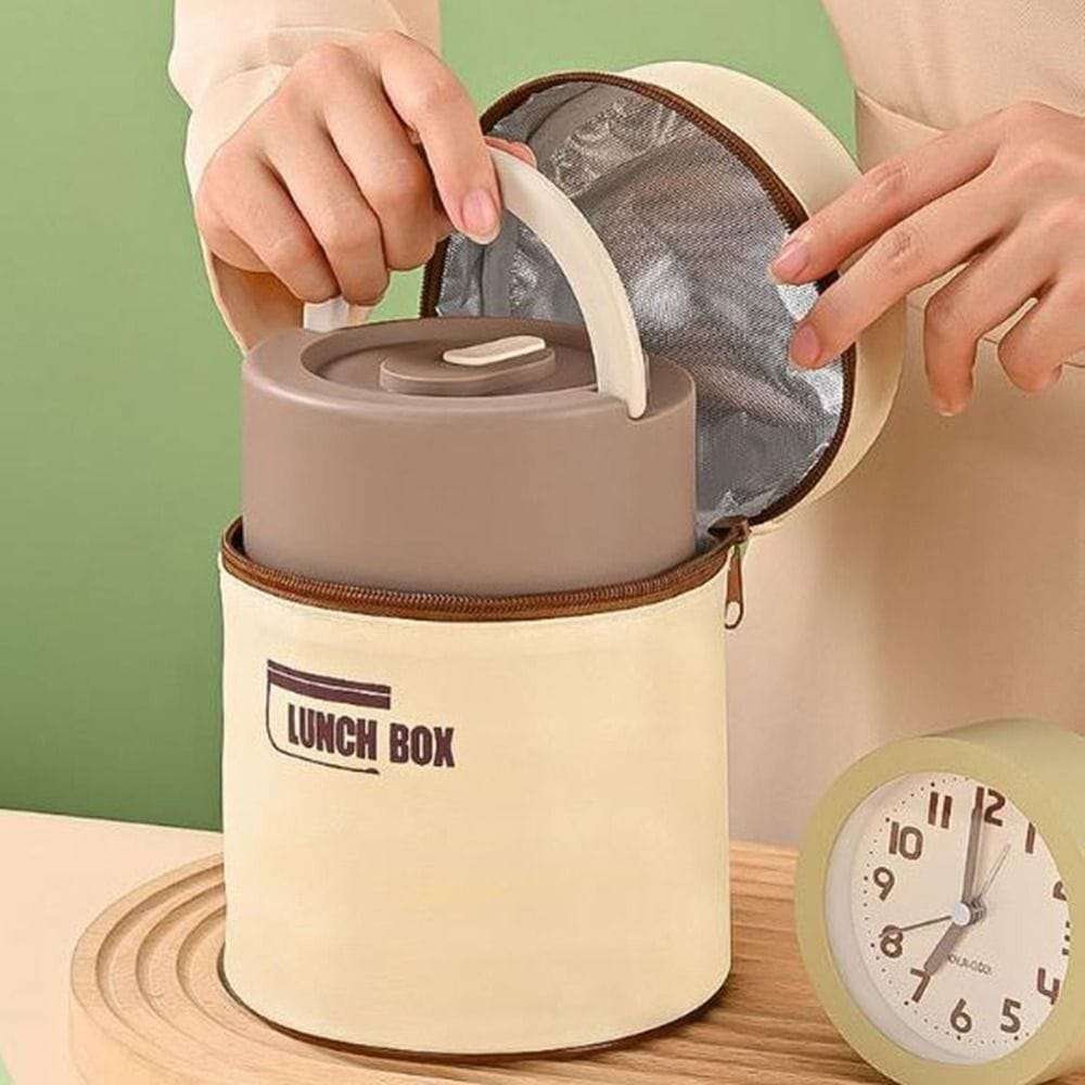Lunch box with beige cover and brown handle, open to reveal a gray interior, on a wooden surface with a green background.