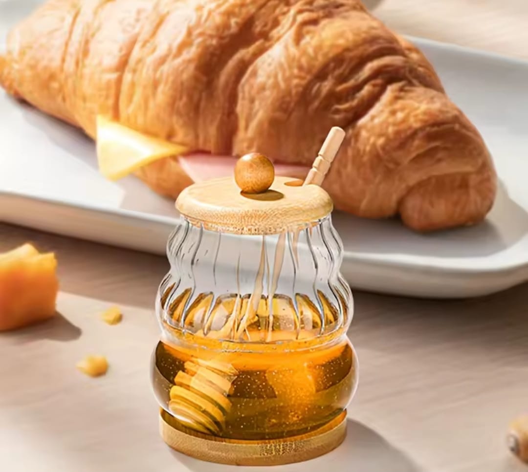 Glass honey dispenser jar with bamboo lid, base, and dipper.