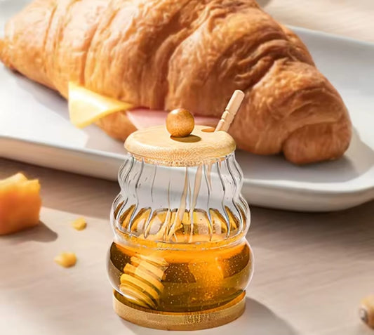 Glass honey dispenser jar with bamboo lid, base, and dipper.